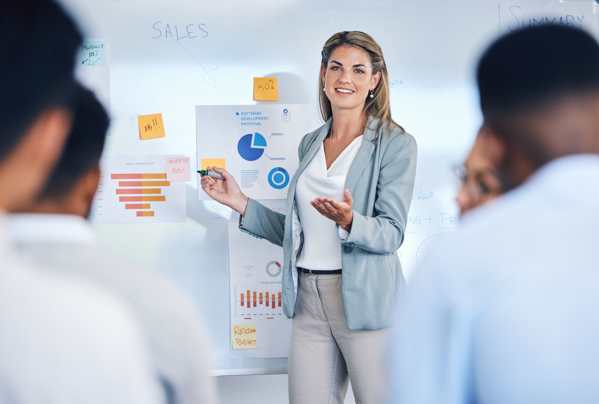 Sales, marketing, lead generation A woman speaker giving a presentation to work crowd. E3 & NLS Sales Training seminar with female present sale analytics and logistics chart on white board